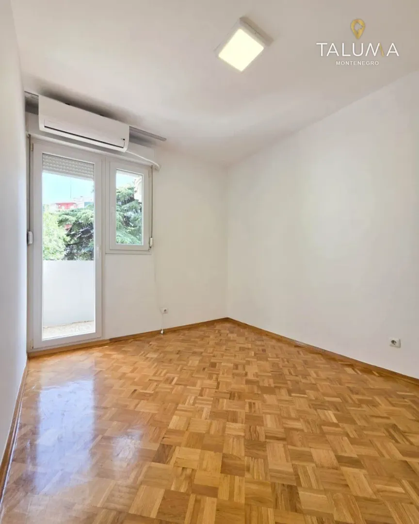 Prazna soba sa parketom i izlazom na balkon.