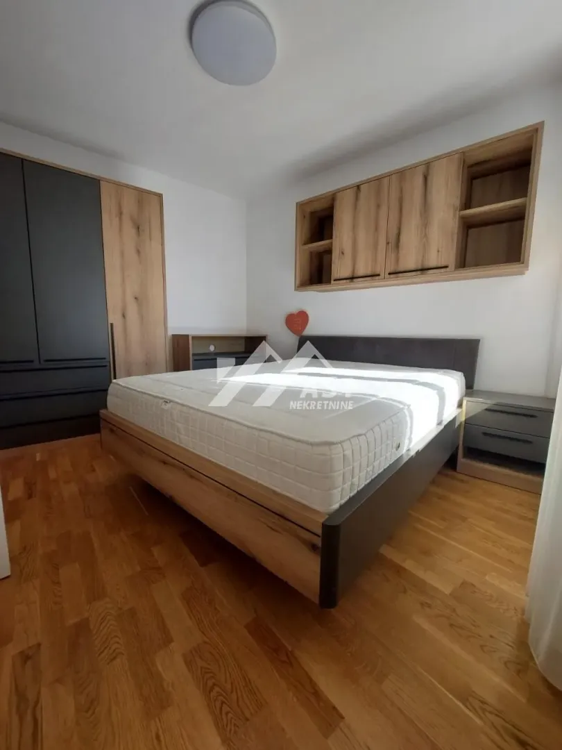 Nameštena spavaća soba sa bračnim krevetom, ormarom i zidnim elementima.