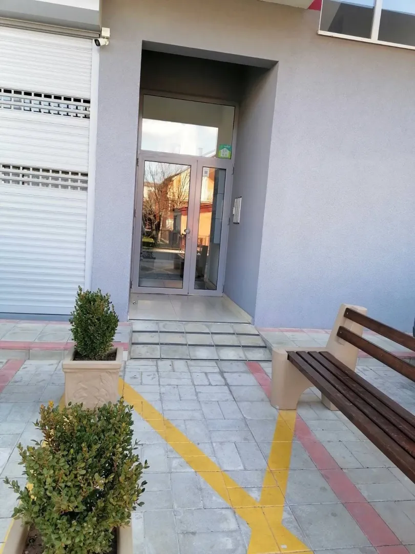 Entrance to a residential building with a paved pathway and a bench.