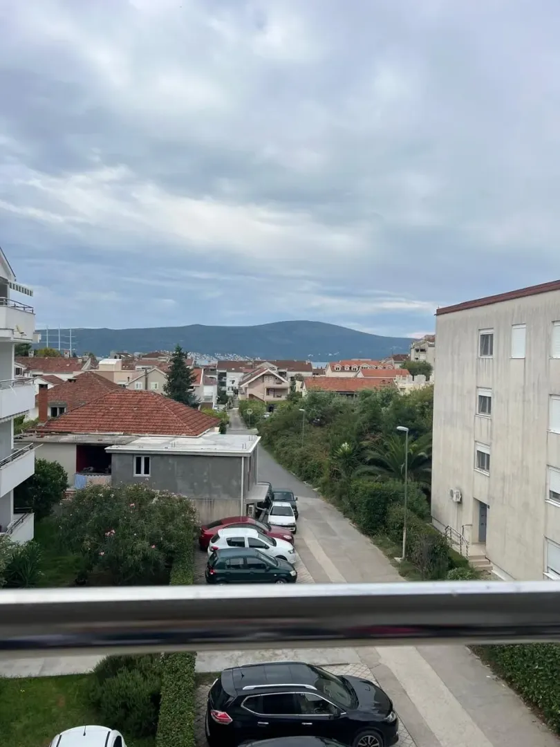 Pogled sa terase na naselje, zelenilo i brda u daljini.