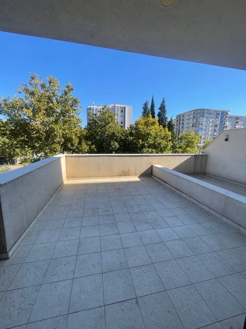 Spacious tiled terrace with a view of the city and surrounding greenery.
