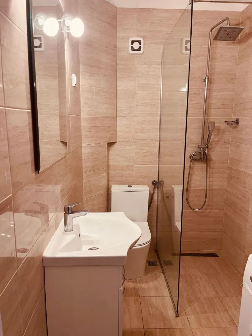 Kupatilo opremljeno umivaonikom, toaletom i tuš kabinom sa staklenom pregradom.