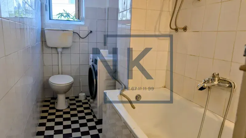 Small bathroom with a bathtub, toilet, and washing machine tiled with ceramic tiles.