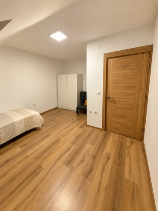Manja spavaća soba sa krevetom, belim garderoberom i drvenim podom.