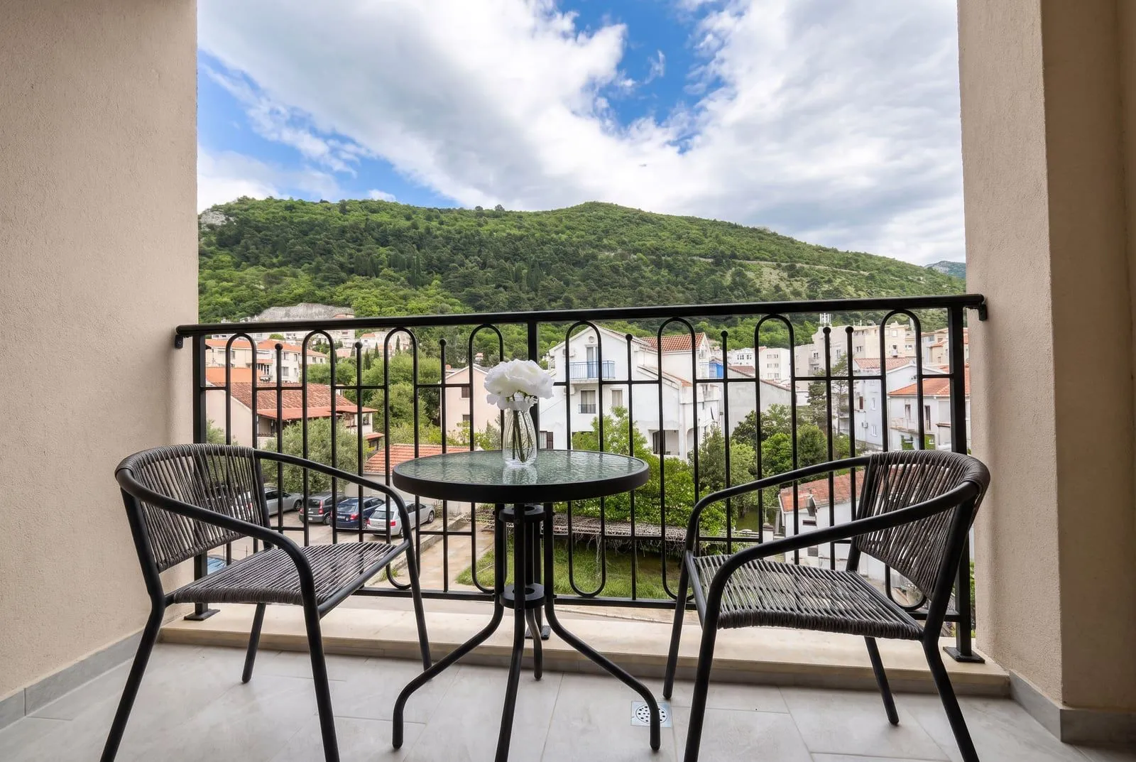 Namješten balkon sa stolom, dvije stolice i pogledom na naselje i brdo.