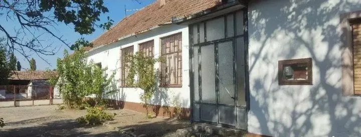 Pogled na dvorište i fasadu starije prizemne kuće sa krovom od crepa.