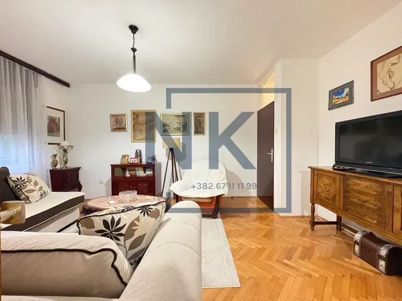 Dnevna soba sa garniturom, TV-om i parketom na podu.