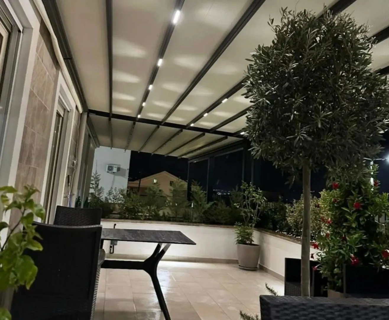 Natkrivena terasa sa garniturom za sedenje i ukrasnim biljkama noću.