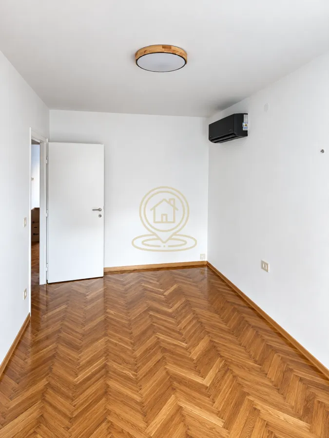 Empty room with parquet flooring and an air conditioning unit.