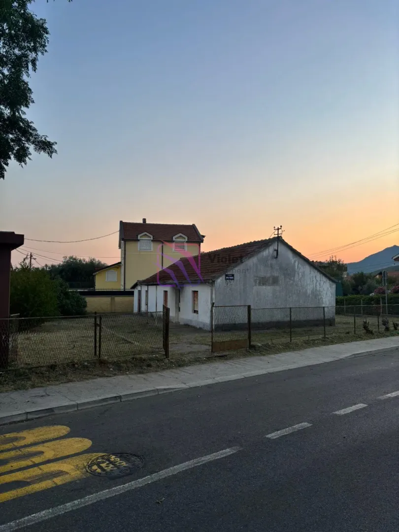 Pogled sa ulice na prizemnu kuću i dvorište u sumrak.
