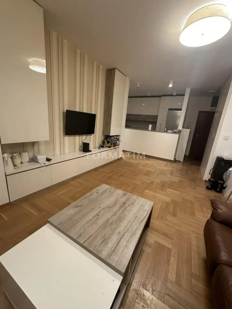 Living room connected to the kitchen, featuring parquet flooring and a TV unit.