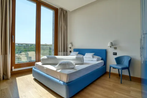 Modern bedroom with a double bed, blue armchair, and large balcony doors. - image 14