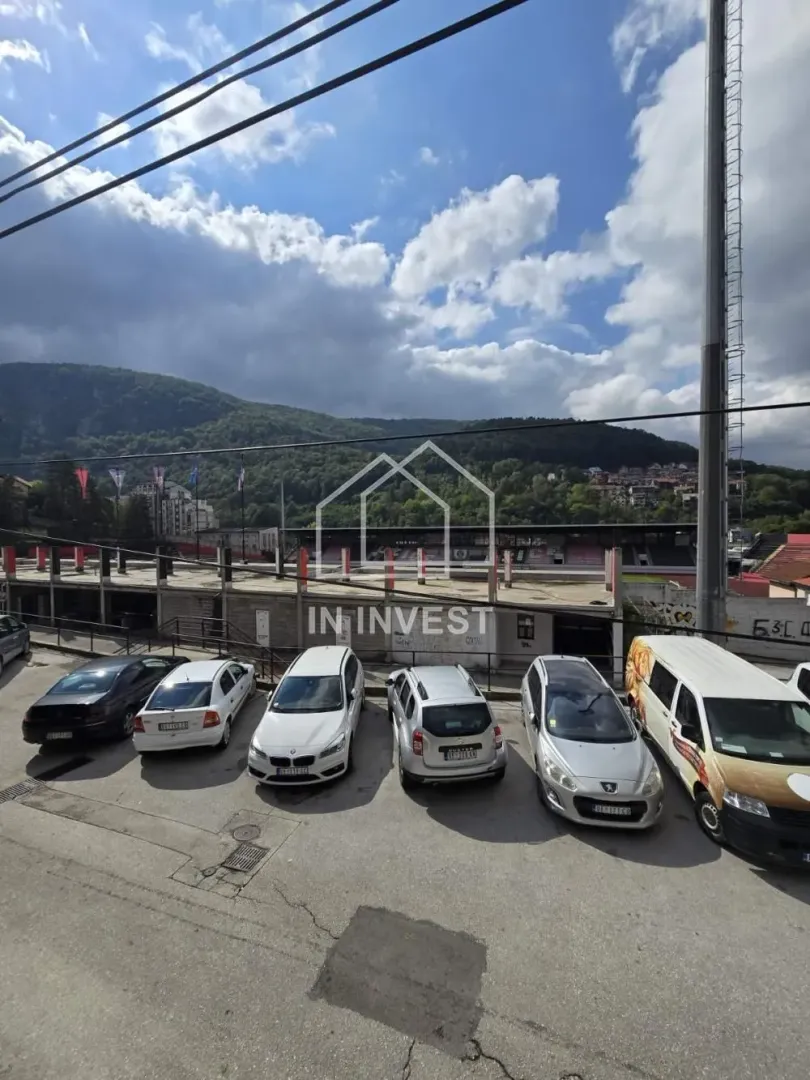 Pogled sa prozora na parking i okolne objekte u prirodi.