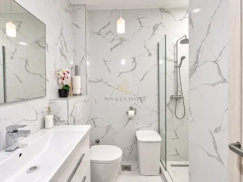 A modern bathroom equipped with marble tiles, a washbasin, and a walk-in shower. - image 11