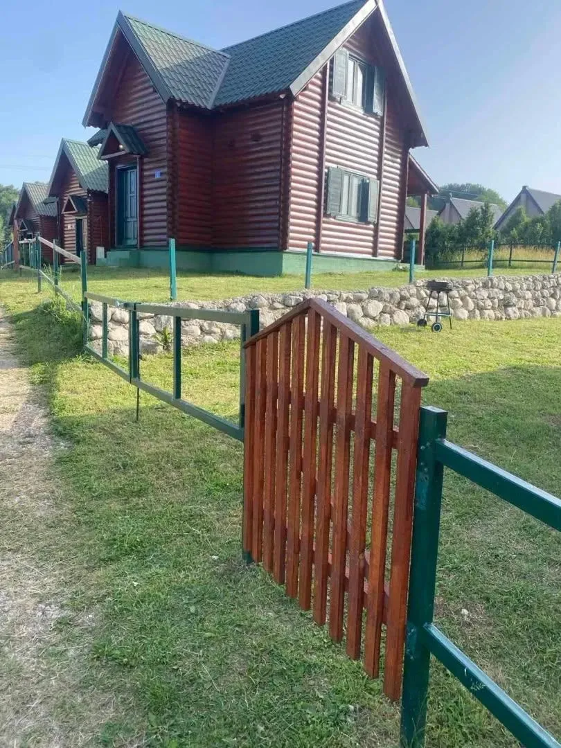 Drvena vikendica sa uređenim dvorištem i ogradom.
