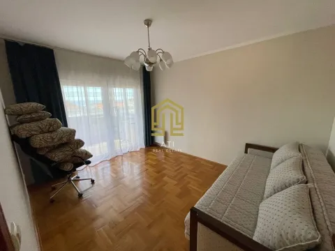 Dnevna soba sa parketom, krevetom i stolicom na kojoj su složeni jastuci. - image 6