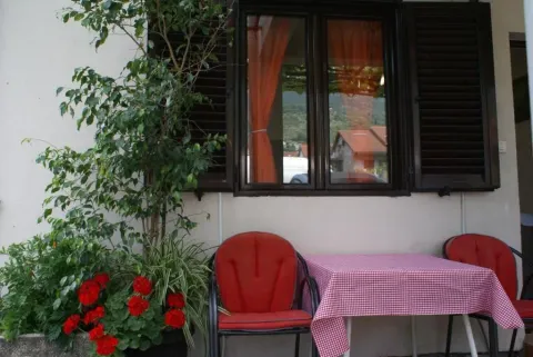 Terasa sa stolom, crvenim stolicama i cvijećem ispred prozora sa roletnama. - image 4