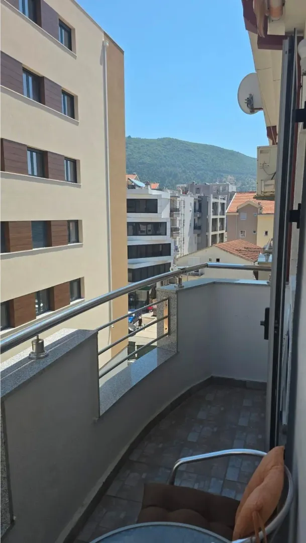 Small balcony with a metal railing and a view of buildings and a hill.