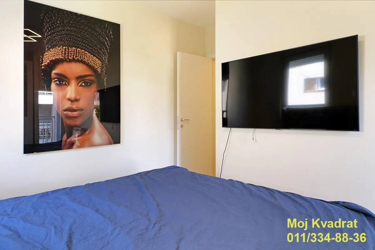 Spavaća soba sa krevetom, velikim televizorom i umetničkom slikom na zidu.