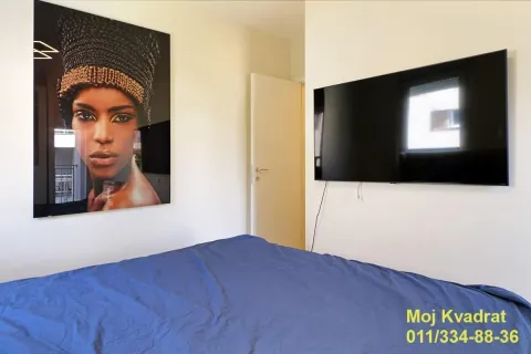 Spavaća soba sa krevetom, velikim televizorom i umetničkom slikom na zidu. - image 7
