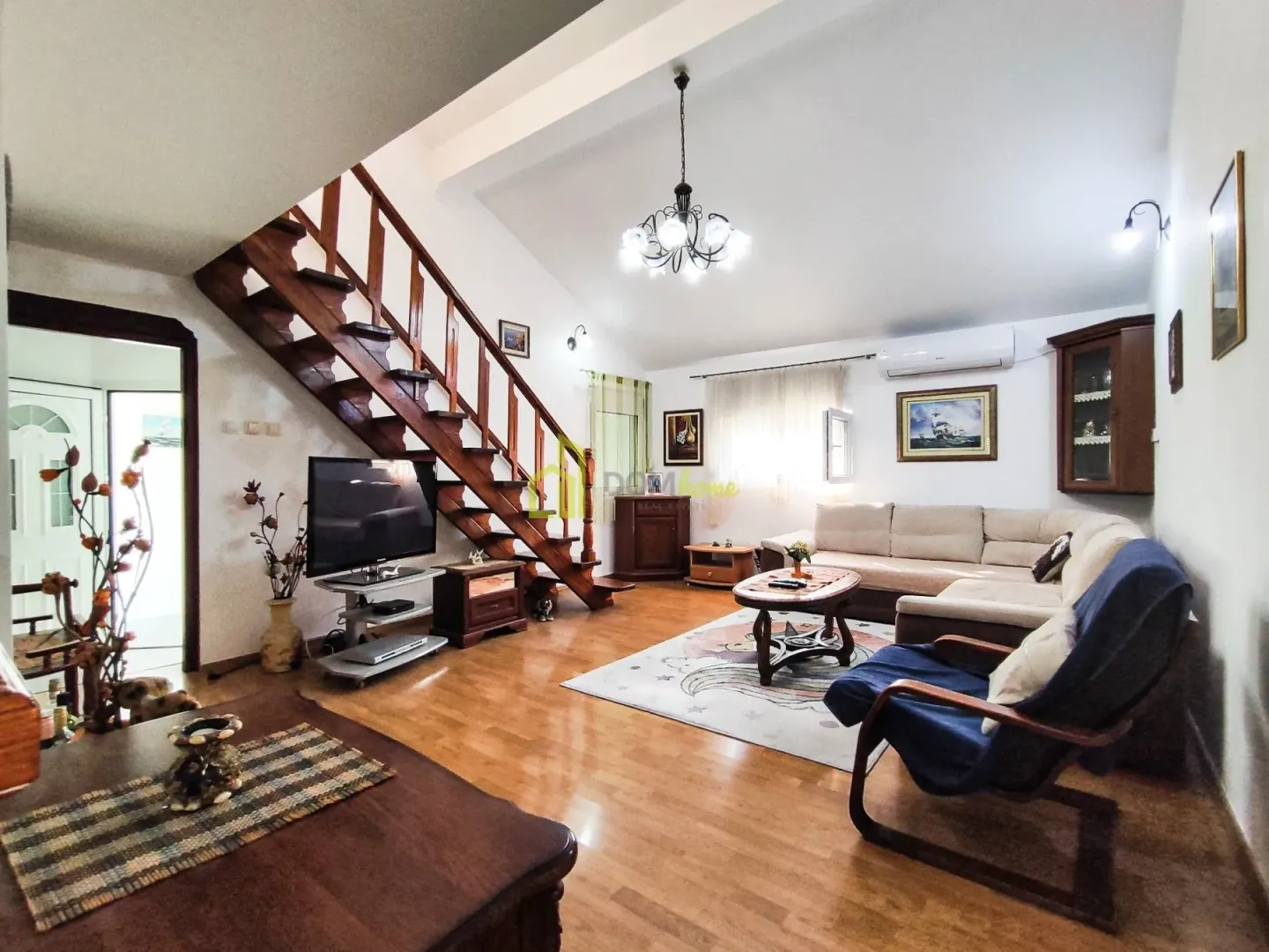 Spacious living room with a sofa set, television, and wooden stairs leading to the upper floor.
