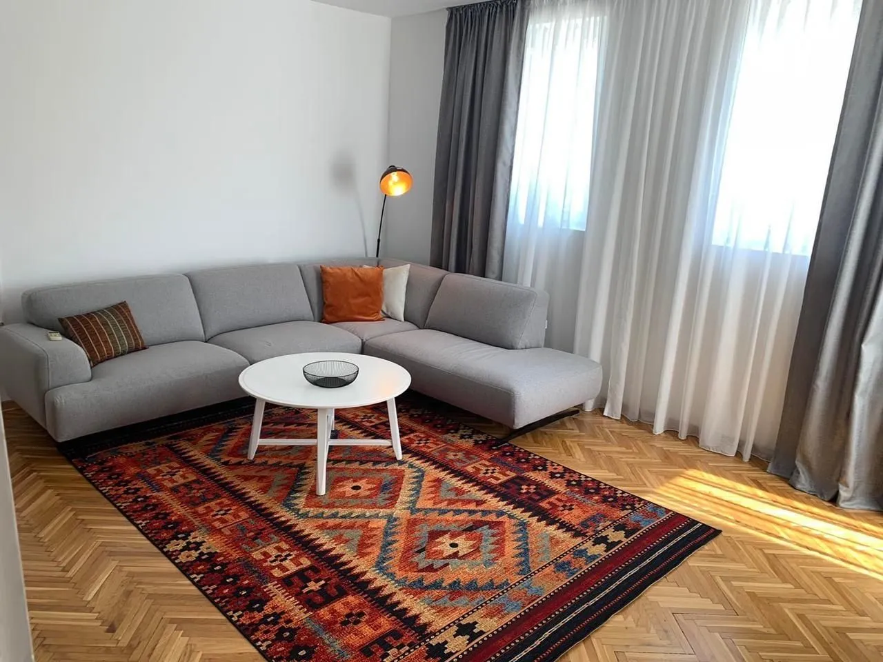 Bright living room with a grey corner sofa and a colorful rug.