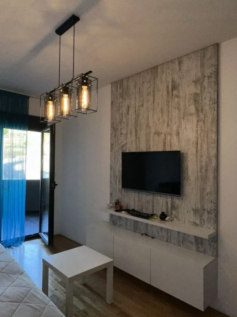 Living room with a TV, white furniture unit, and modern pendant light.