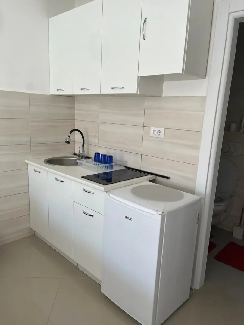 Manja bijela kuhinja sa sudoperom, pločom i frižiderom.