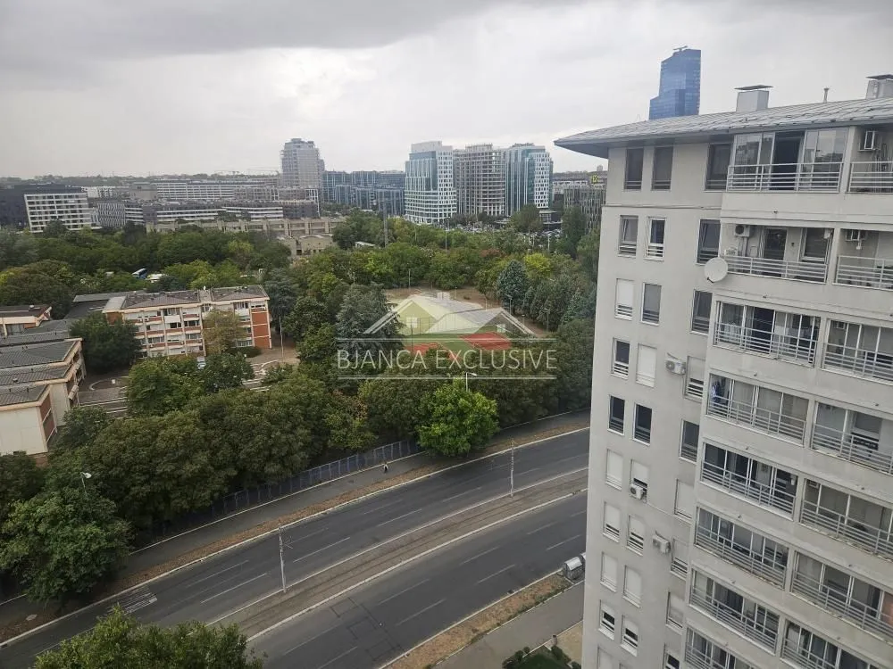 Pogled sa prozora na okolne zgrade, zelene površine i gradsku ulicu.