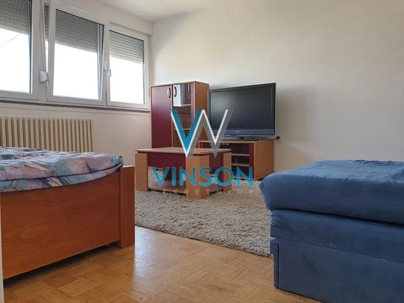Nameštena dnevna soba sa televizorom i drvenim nameštajem.