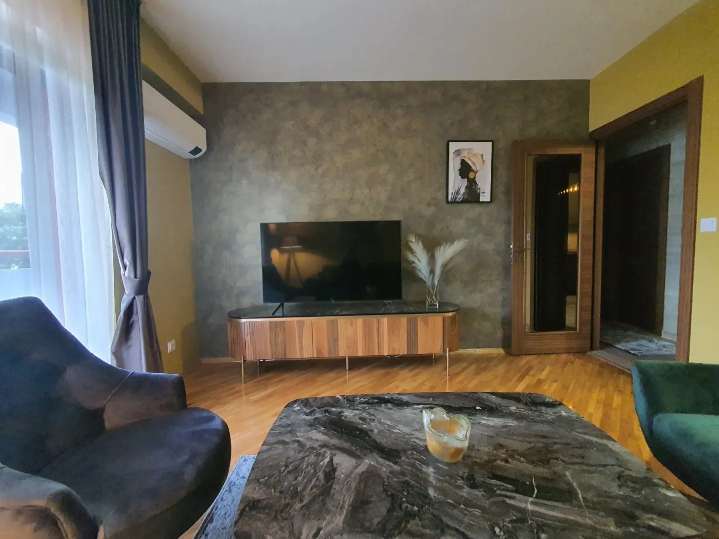 Dnevna soba sa televizorom, drvenom komodom i modernim foteljama.