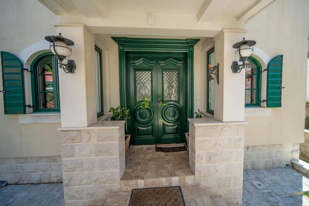 Main entrance of the house with wooden doors and green window shutters.
