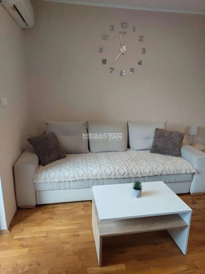 Dnevna soba sa ugaonom garniturom, stočićem i zidnim satom.