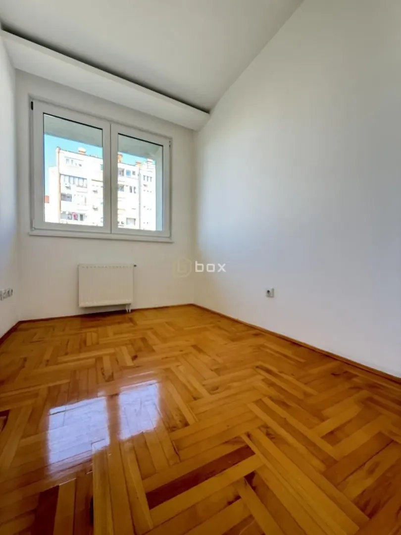Empty room with parquet flooring and a window overlooking the neighboring building.
