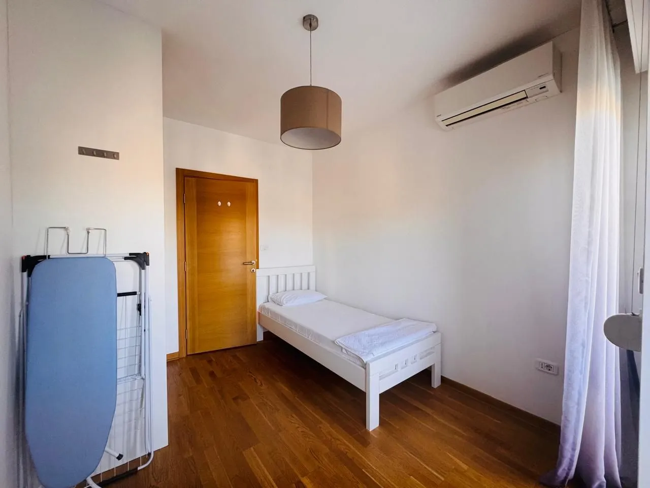 Manja spavaća soba sa krevetom za jednu osobu, drvenim podom i klima uređajem.