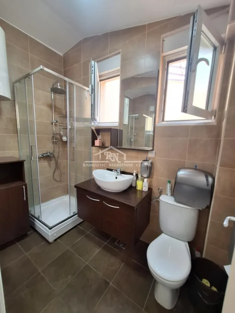 Kupatilo opremljeno tuš kabinom, umivaonikom sa ormarićem i toaletom.