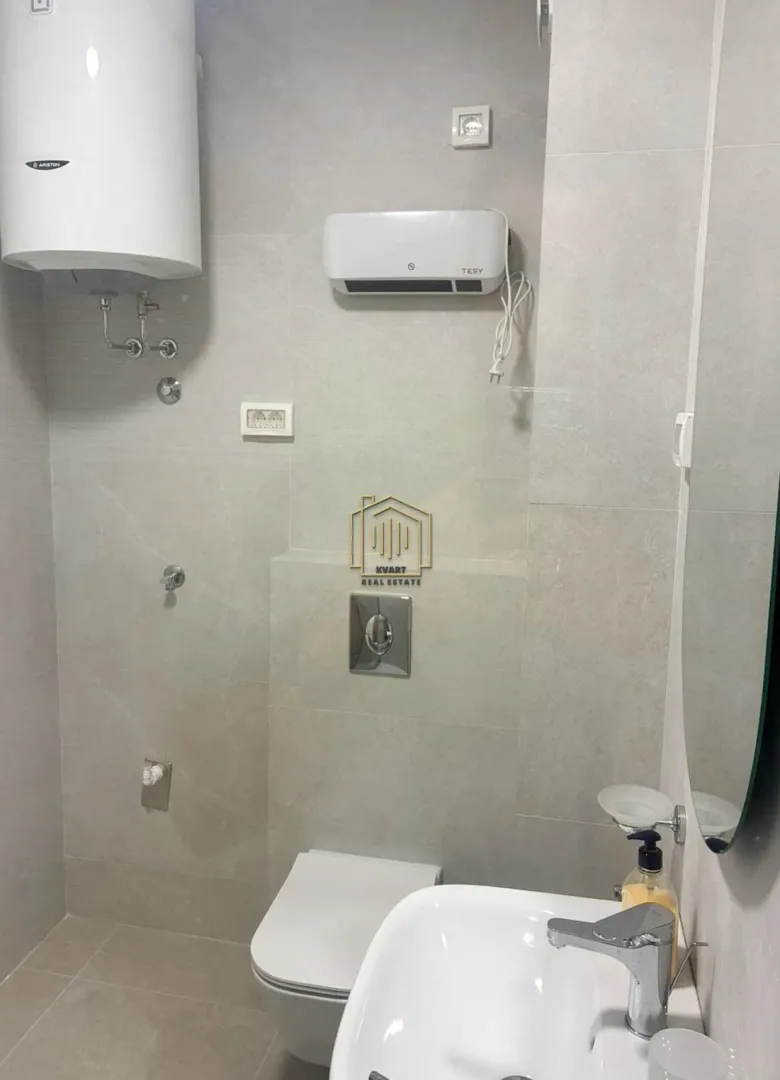 Modern bathroom with neutral-toned tiles, toilet, washbasin, and water heater.