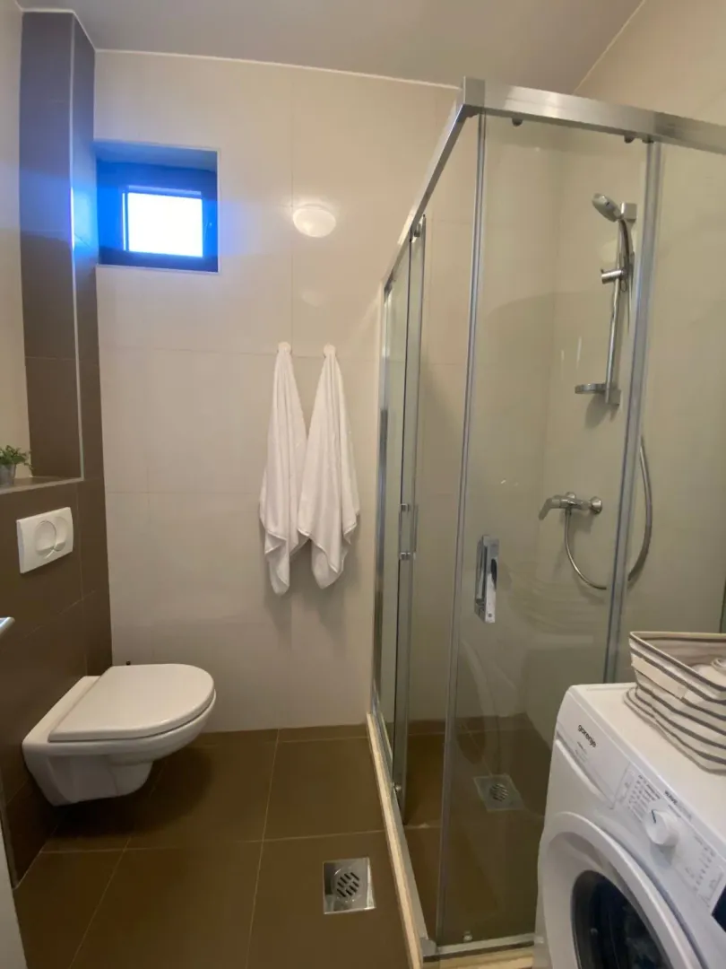 Moderne kupatilo sa tuš kabinom, WC šoljom i veš mašinom.