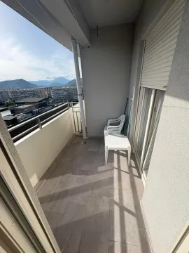 Long covered balcony with a plastic table and chairs and a city view. - image 5