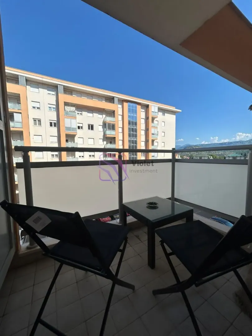 Namješten balkon sa stolom i stolicama i pogledom na okolne zgrade.