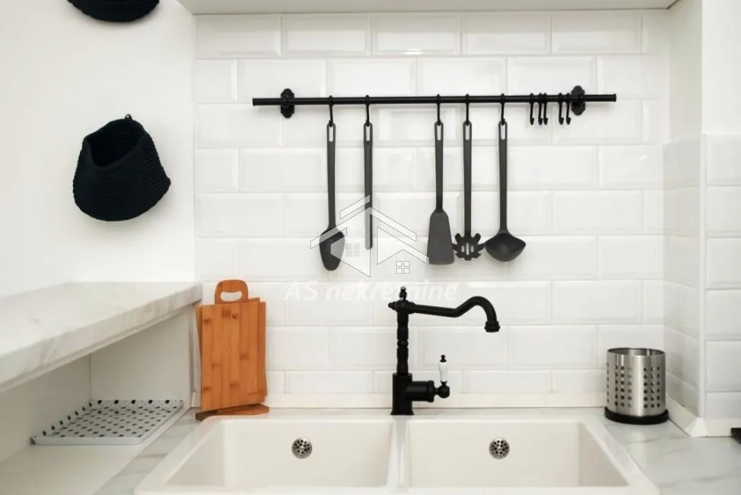 Kitchen sink with a black faucet and utensils on the wall.