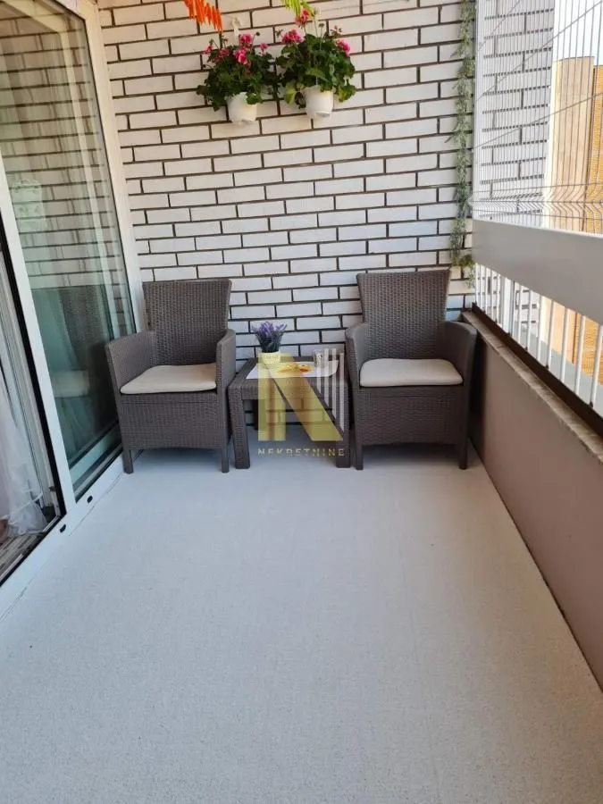 Manji namešten balkon sa garniturom za sedenje i ukrasnim cvećem na zidu.