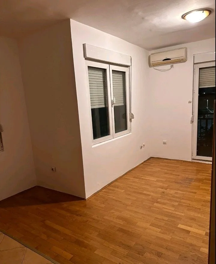 An empty, bright room with wooden flooring and an air conditioning unit.