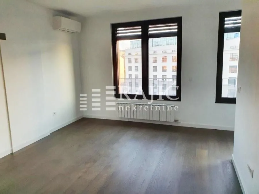 Empty room with parquet flooring and large windows.