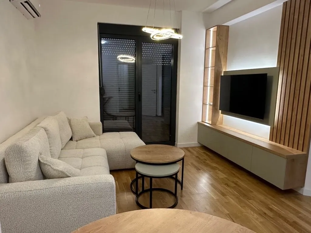 Dnevna soba sa ugaonom garniturom, TV komodom i drvenim oblogama na zidu.
