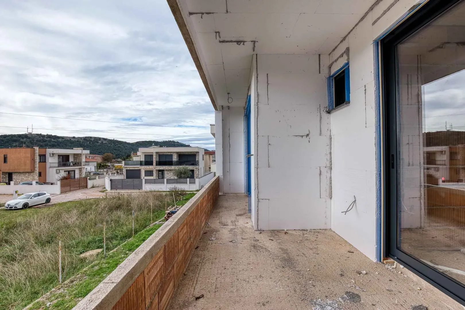 Nezavršen balkon sa pogledom na naselje i okolna brda.