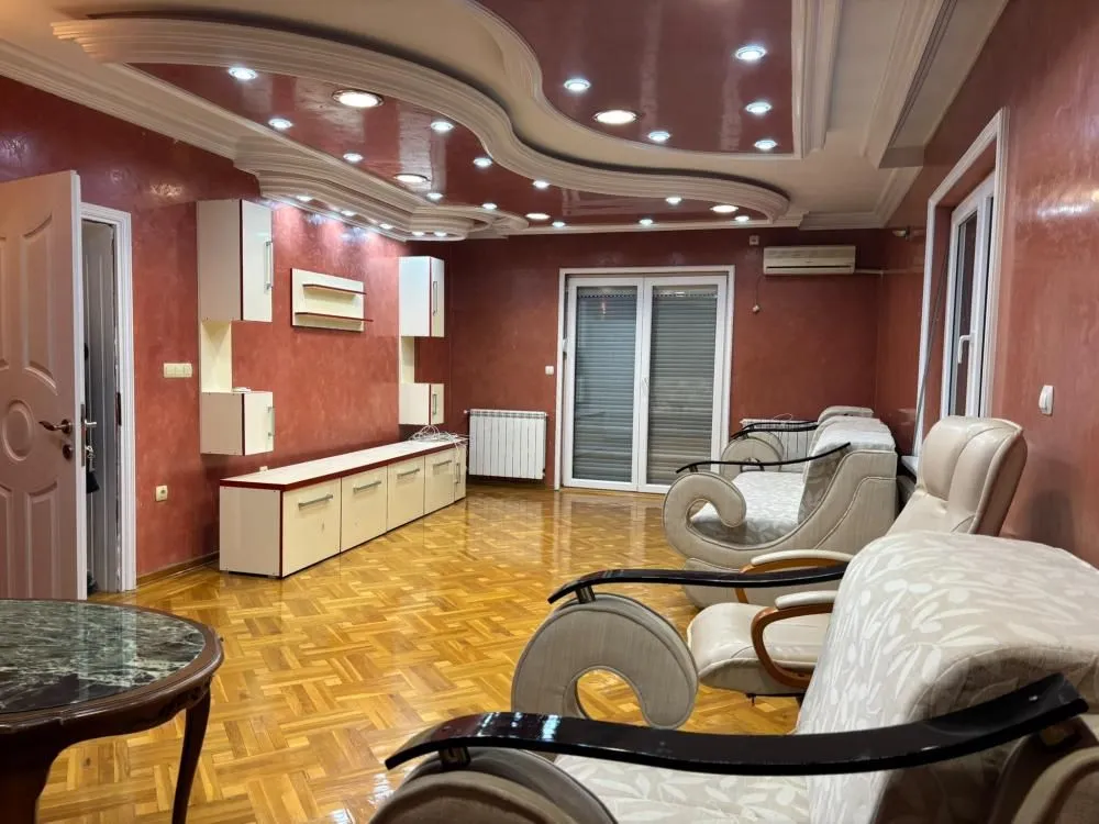 Spacious living room with seating furniture and a dropped ceiling with lighting.