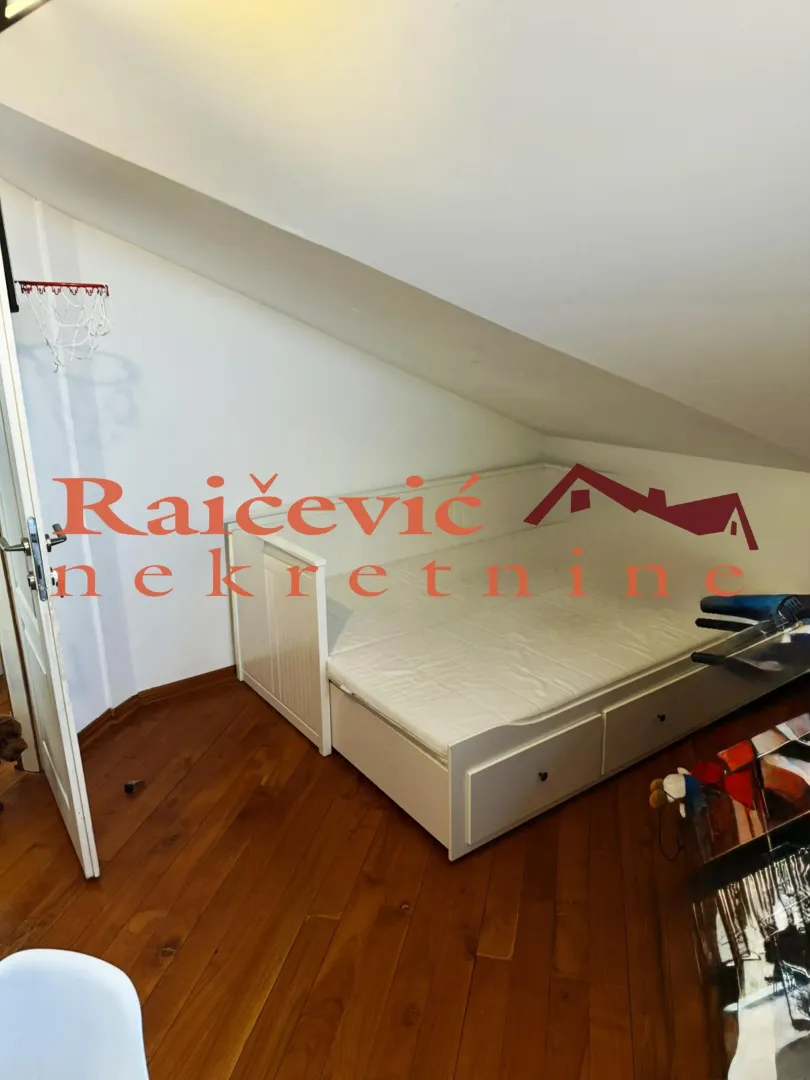 Attic bedroom with a white bed and wooden flooring.