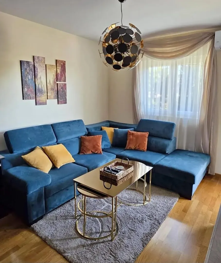 Dnevna soba sa plavom ugaonom garniturom, stočićem i ukrasnim detaljima.
