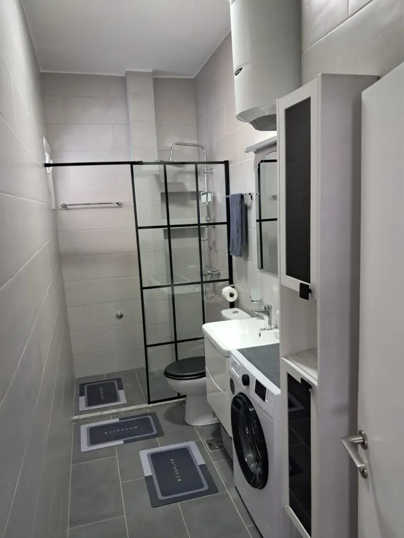 Modernly equipped bathroom with a walk-in shower, washbasin, and washing machine.